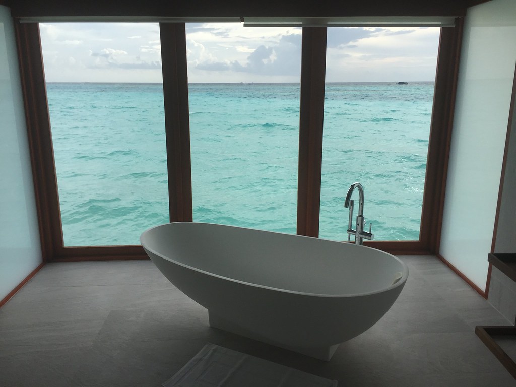 Sculptural freestanding stone bathtub facing a full-height window over open water