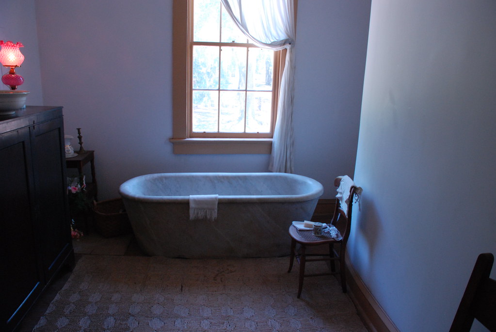 Hand-honed grey stone bathtub with a rolled rim, beside a tall window